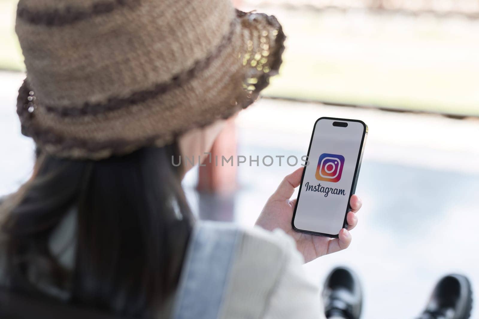 CHIANG MAI, THAILAND - JAN 18 2024: A woman holds Apple iPhone 14 with Instagram application on the screen at cafe. Instagram is a photo-sharing app for smartphones.