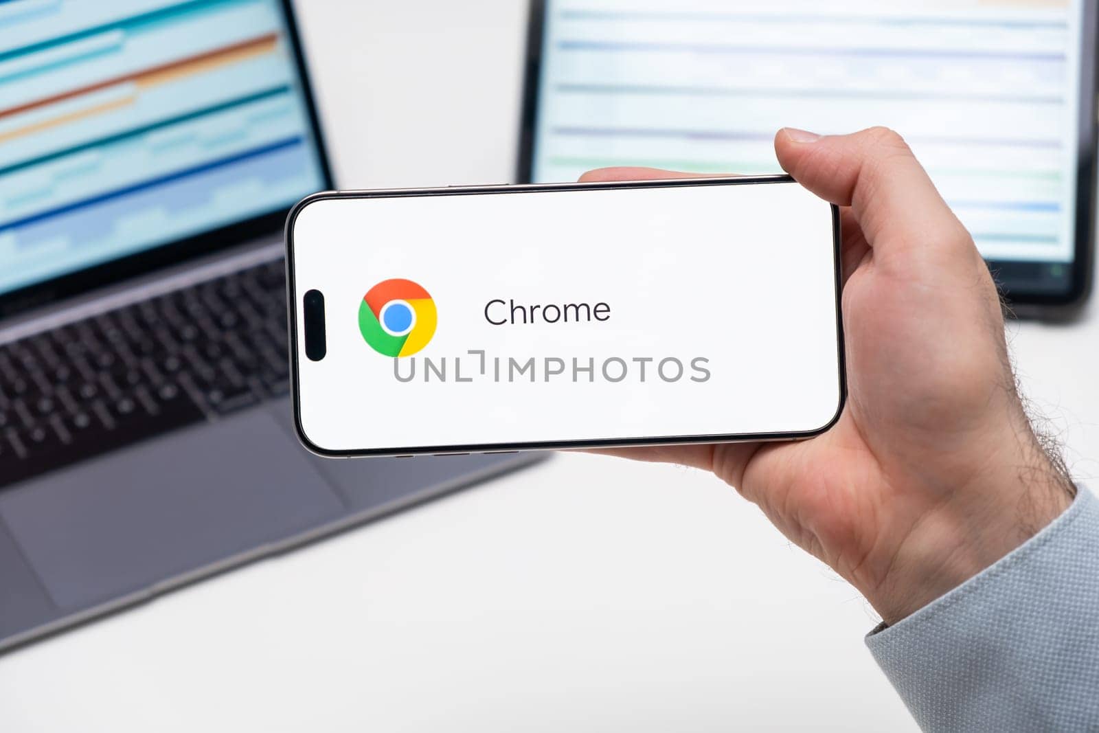 Chrome application logo on the screen of smart phone in mans hand, laptop and tablet are on the table in the background, December 2023, Prague, Czech Republic.
