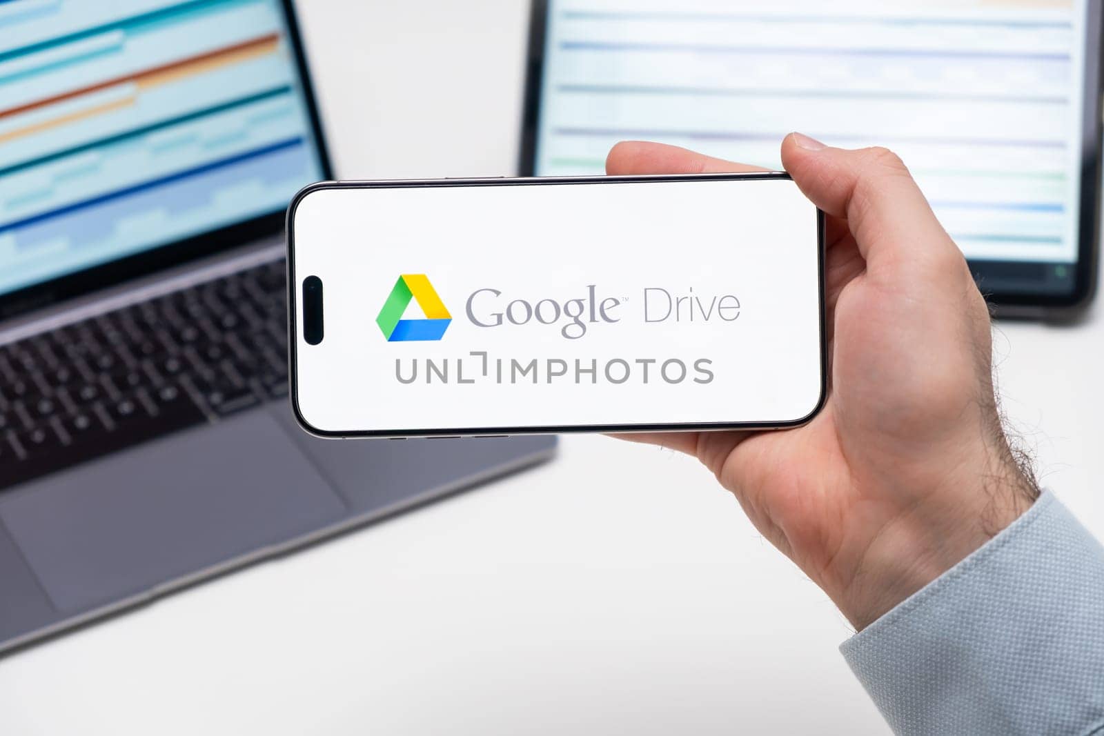 Google Drive logo of app on the screen of mobile phone held by man in front of the laptop and tablet by vladimka