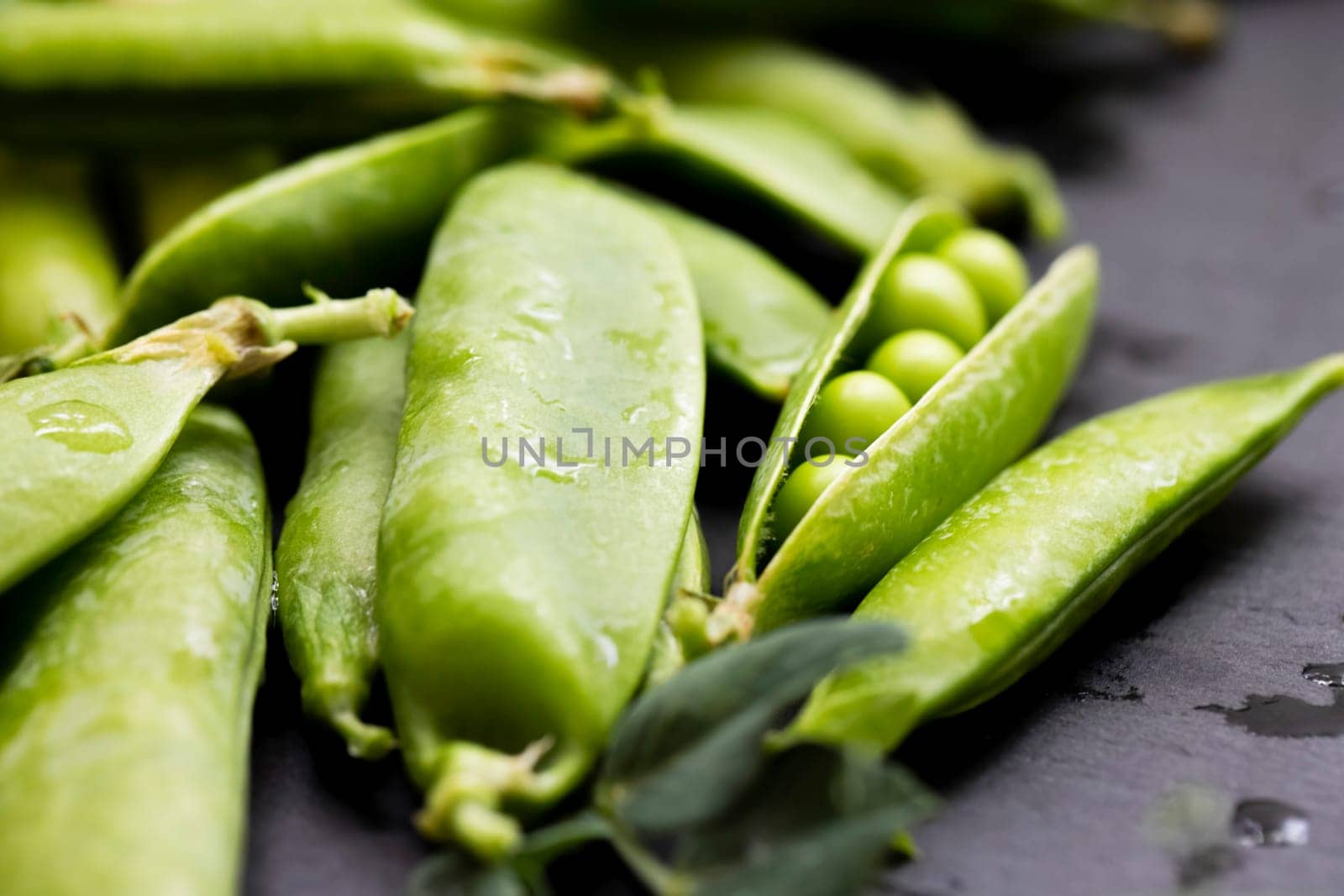 Macro shot of vibrant green pea pods with glistening water droplets, showcasing the freshness and natural texture of the legumes