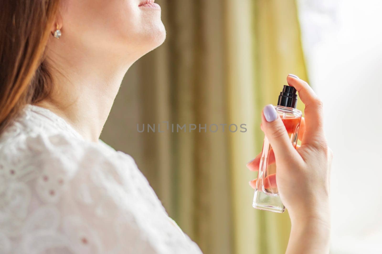 Woman in white blouse with eyes closed, enjoying the scent of a perfume bottle, evoking a sense of luxury and personal care