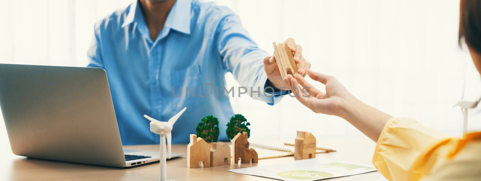 Two business people talking about eco city at green business meeting on meeting table with windmill represented renewable energy, wooden house block and tree model represent green city. Delineation.
