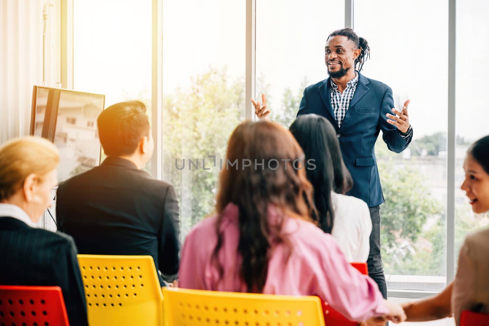 Businesspeople from diverse backgrounds gather for a meeting in an office. Managers attentively listen to their team's ideas as they sit, surrounded by colleagues in chairs.