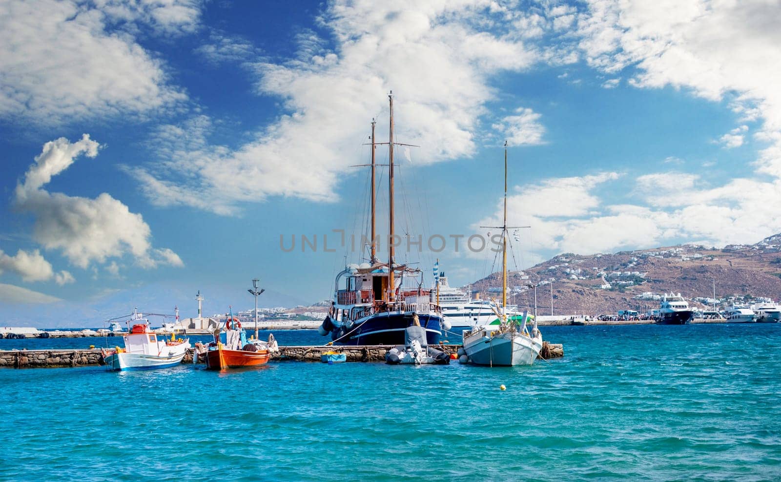 Icredible view of sailing yachts and boats moored to the stone pier on the tranquiose sea bay and mountanious landscape of greece island