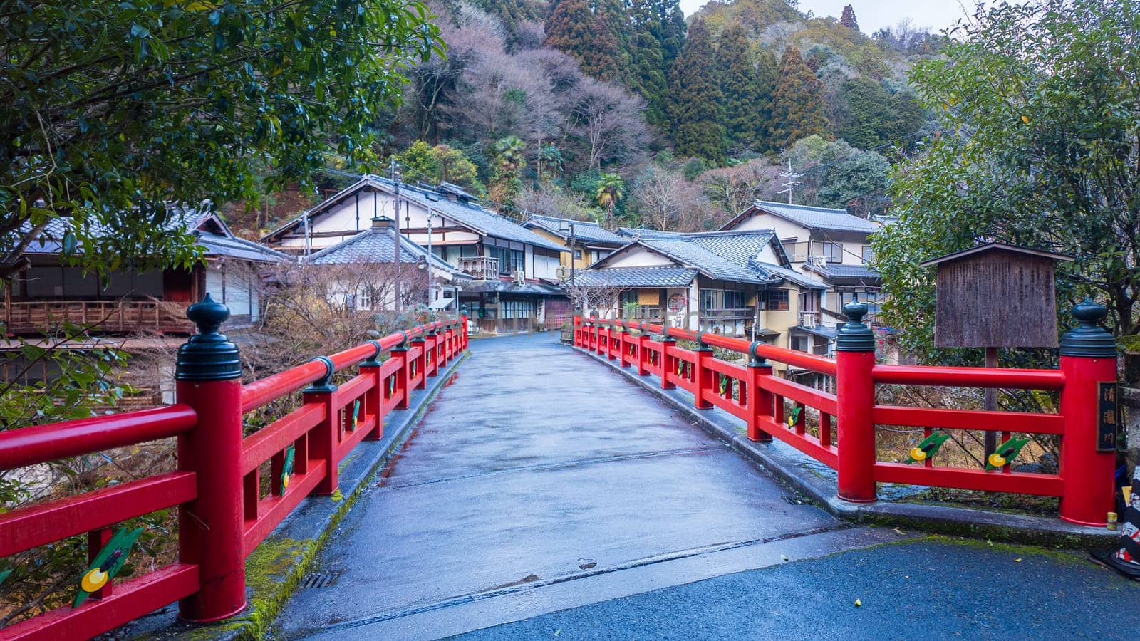 Red traditional Japanese bridge to small village in forested mountains. High quality photo