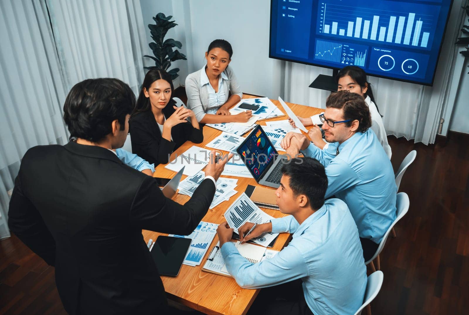 Diverse group of business analyst team analyzing financial data report. Finance data analysis chart and graph dashboard show on TV screen in meeting room for strategic marketing planning. Habiliment