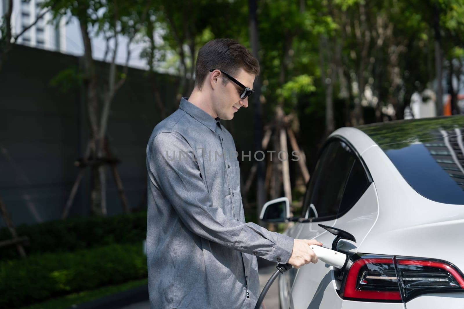 Young man travel with EV electric car in green sustainable city innards by biancoblue