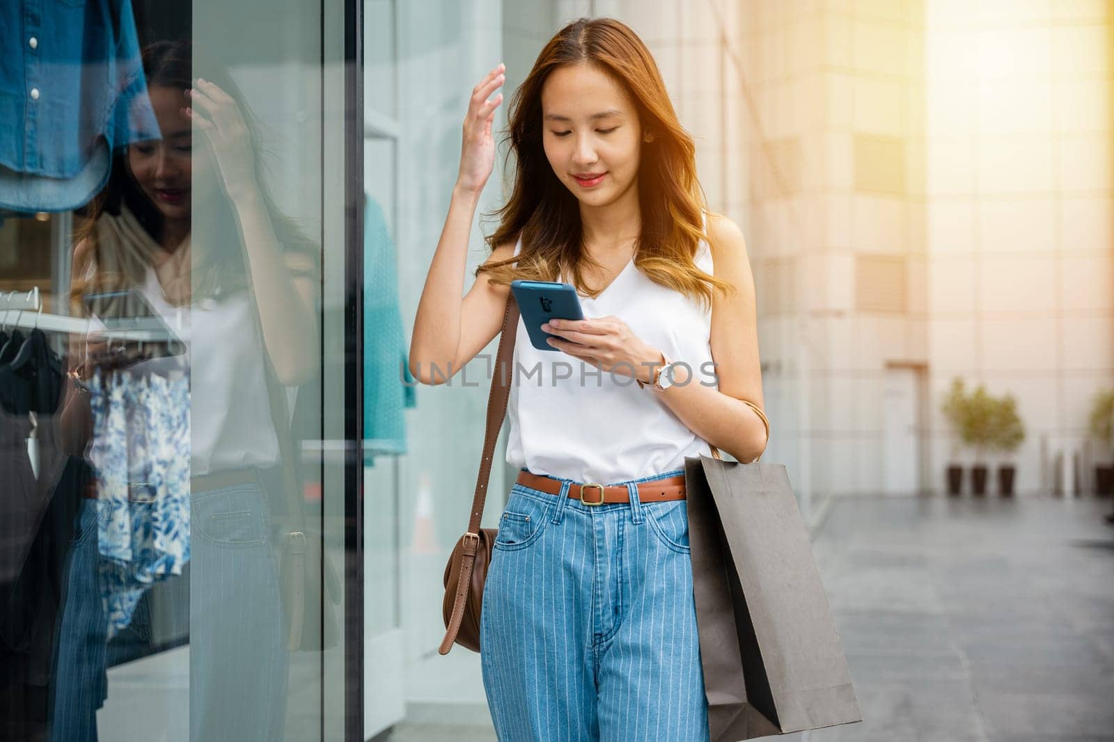 Young woman scrolling through her smartphone while standing against a wall in the city. Her phone is her window to the virtual world of social media and entertainment.