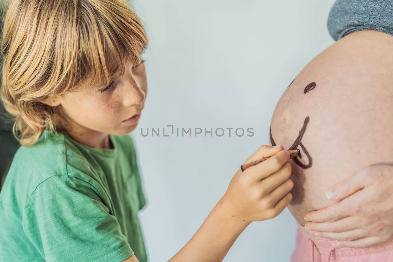 Adorable moment as a son adds a touch of joy to his mother's pregnancy, playfully drawing a funny face on her baby bump, creating cherished memories by galitskaya