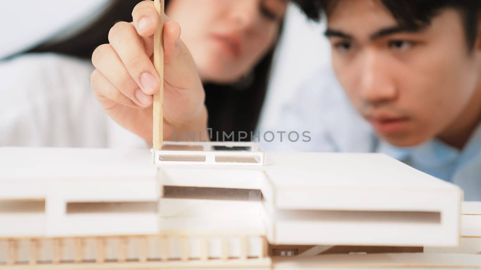 Closeup of young professional architect team work together to use pencil testing house model durability about house construction. Creative design and teamwork concept. Focus on hand. Immaculate.