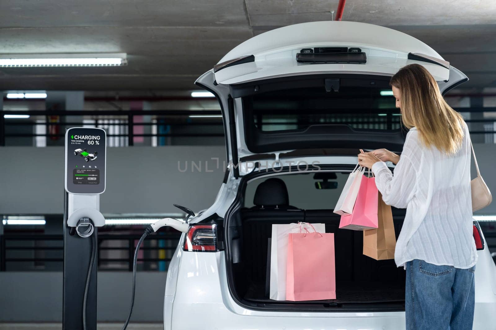 Young woman travel with EV electric car to shopping center parking lot charging in downtown city showing urban sustainability lifestyle by green clean rechargeable energy of electric vehicle innards