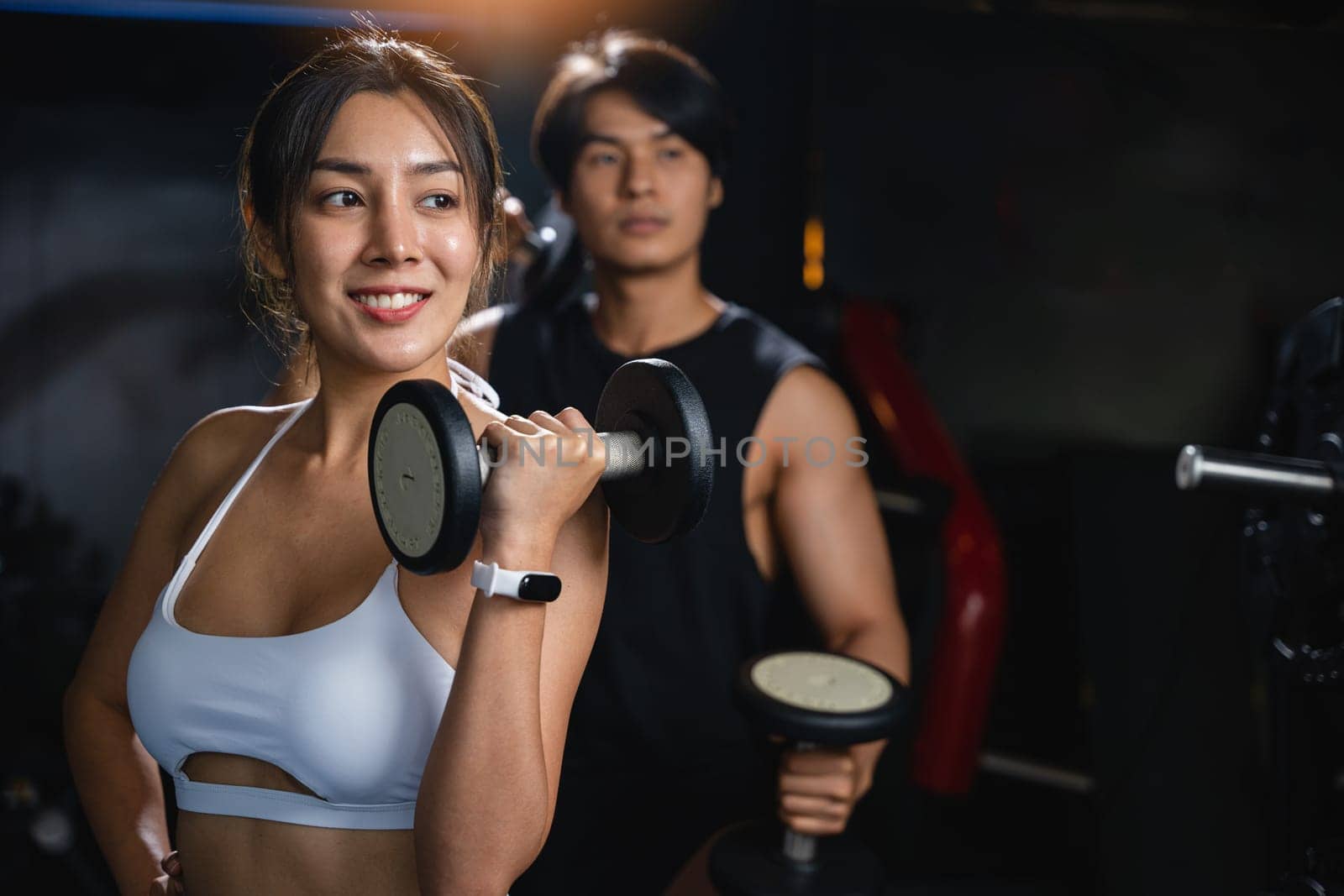 A fit couple in black workout clothes, smiling cheerfully while holding dumbbells, works together to build their muscular bodies and achieve their fitness goals. lifestyle fitness concept