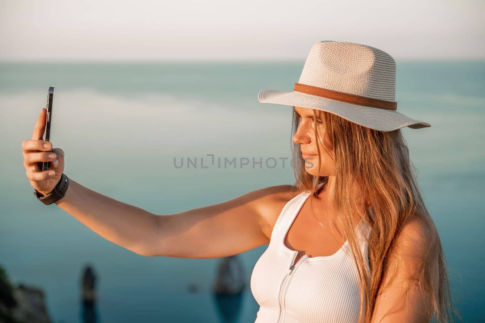 Selfie woman in hat, white tank top and shorts makes selfie shot mobile phone post photo social network outdoors on sea background beach people vacation lifestyle travel concept