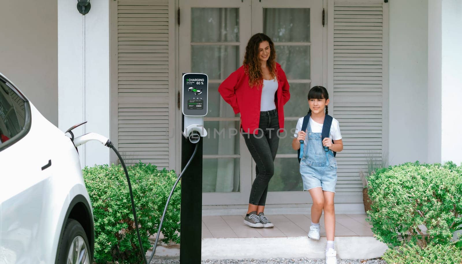 Little young girl help her mother recharge EV car at home. Synchronos by biancoblue