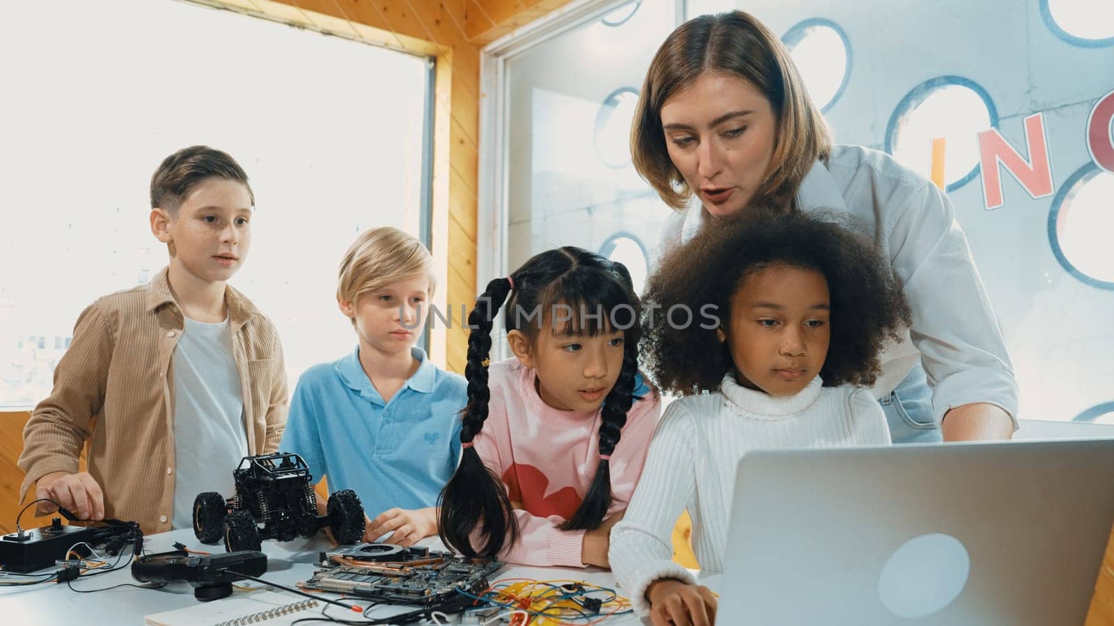 Caucasian teacher praise student while looking at learner work or presentation. Group of diverse student looking at presentation and fixing motherboard at table with chips and wires placed. Erudition.