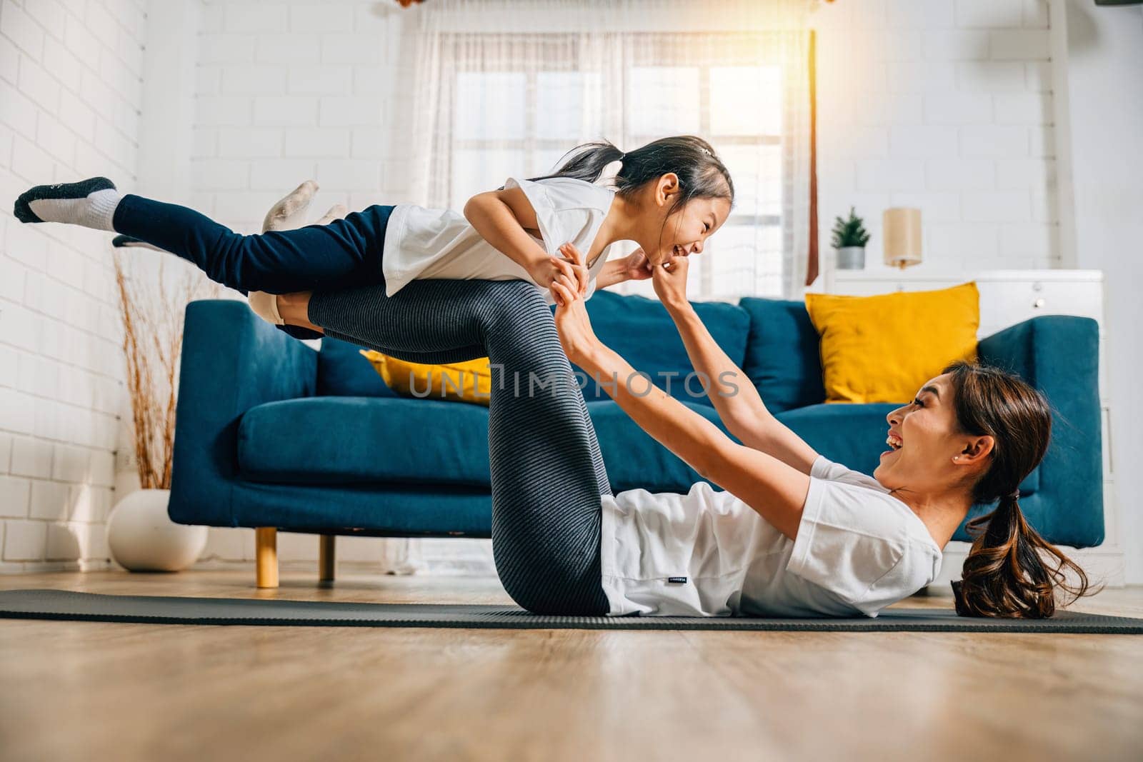 A harmonious family practices the little bird posture in yoga at home. The mother's support and the daughter's joy create a joyful and harmonious moment filled with trust happiness and togetherness.