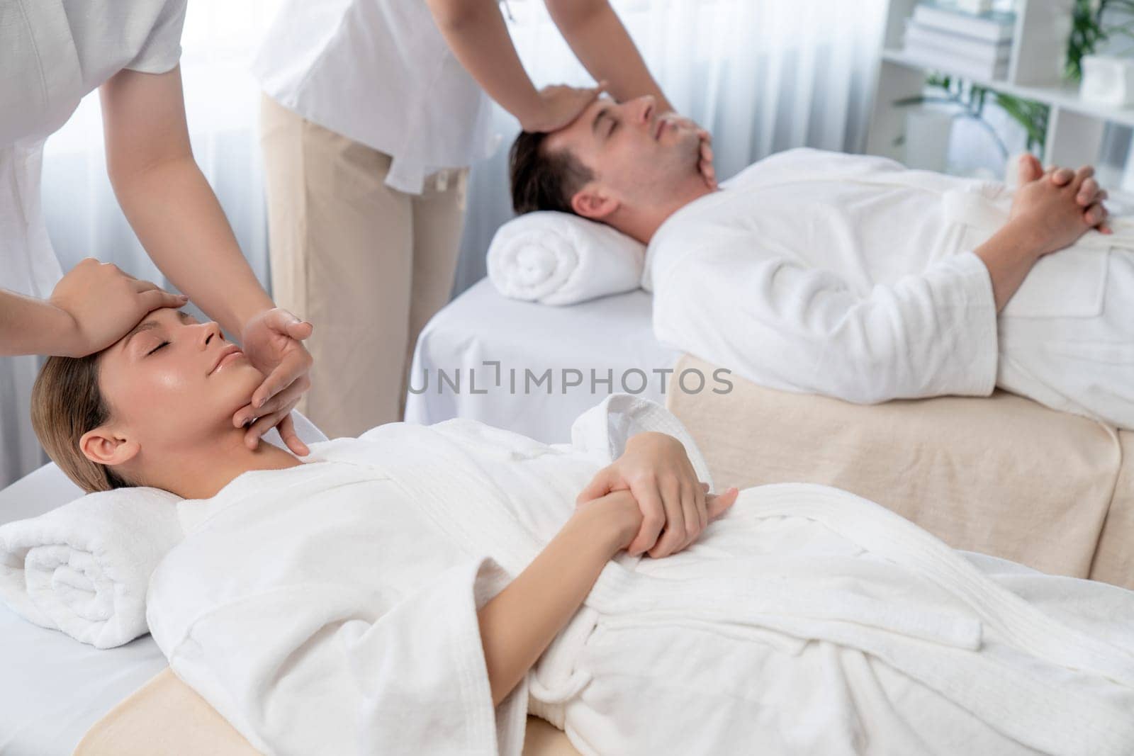 Caucasian couple enjoying relaxing anti-stress head massage and pampering facial beauty skin recreation leisure in dayspa modern light ambient at luxury resort or hotel spa salon. Quiescent