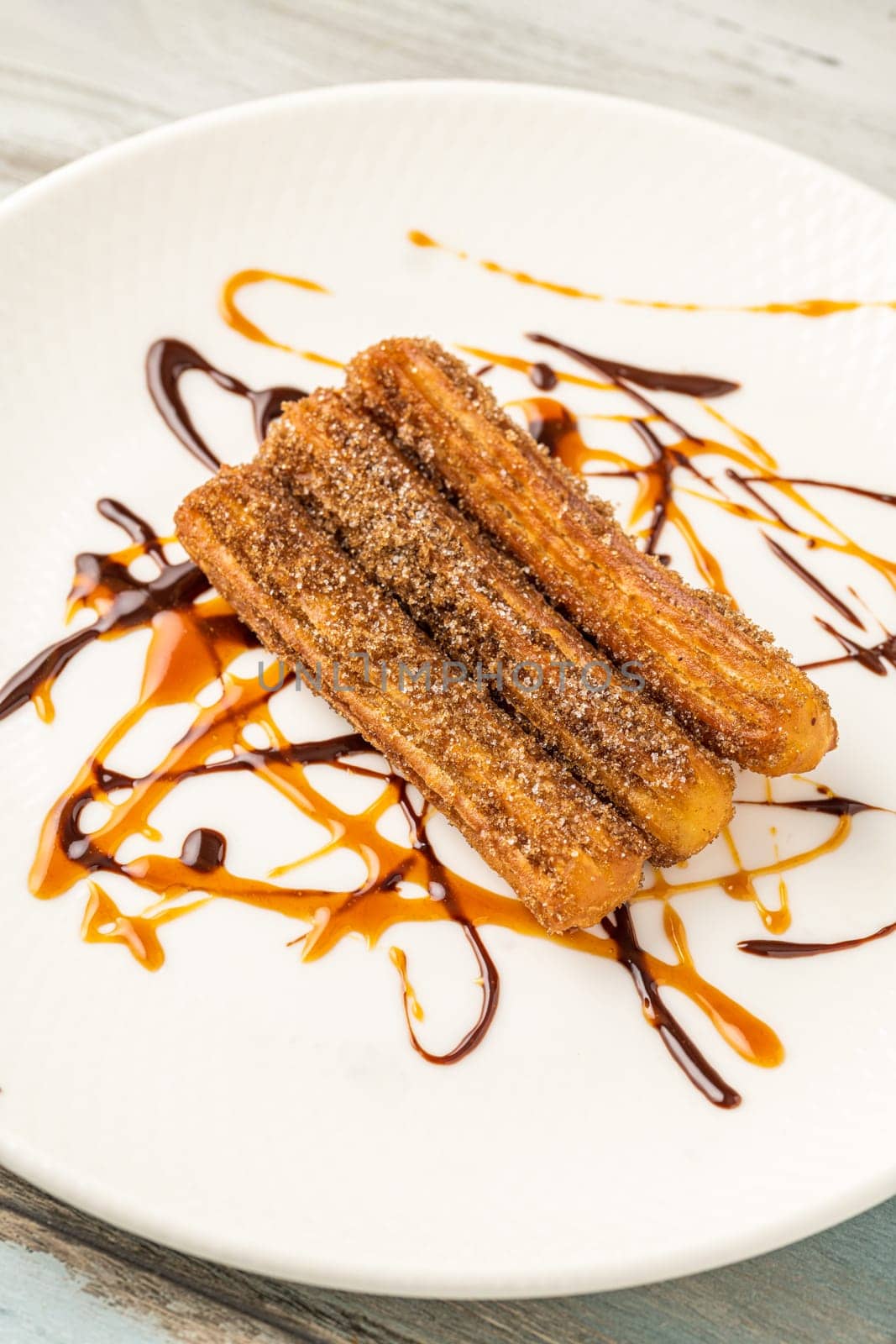 Hot churros with chocolate sauce on wooden table.