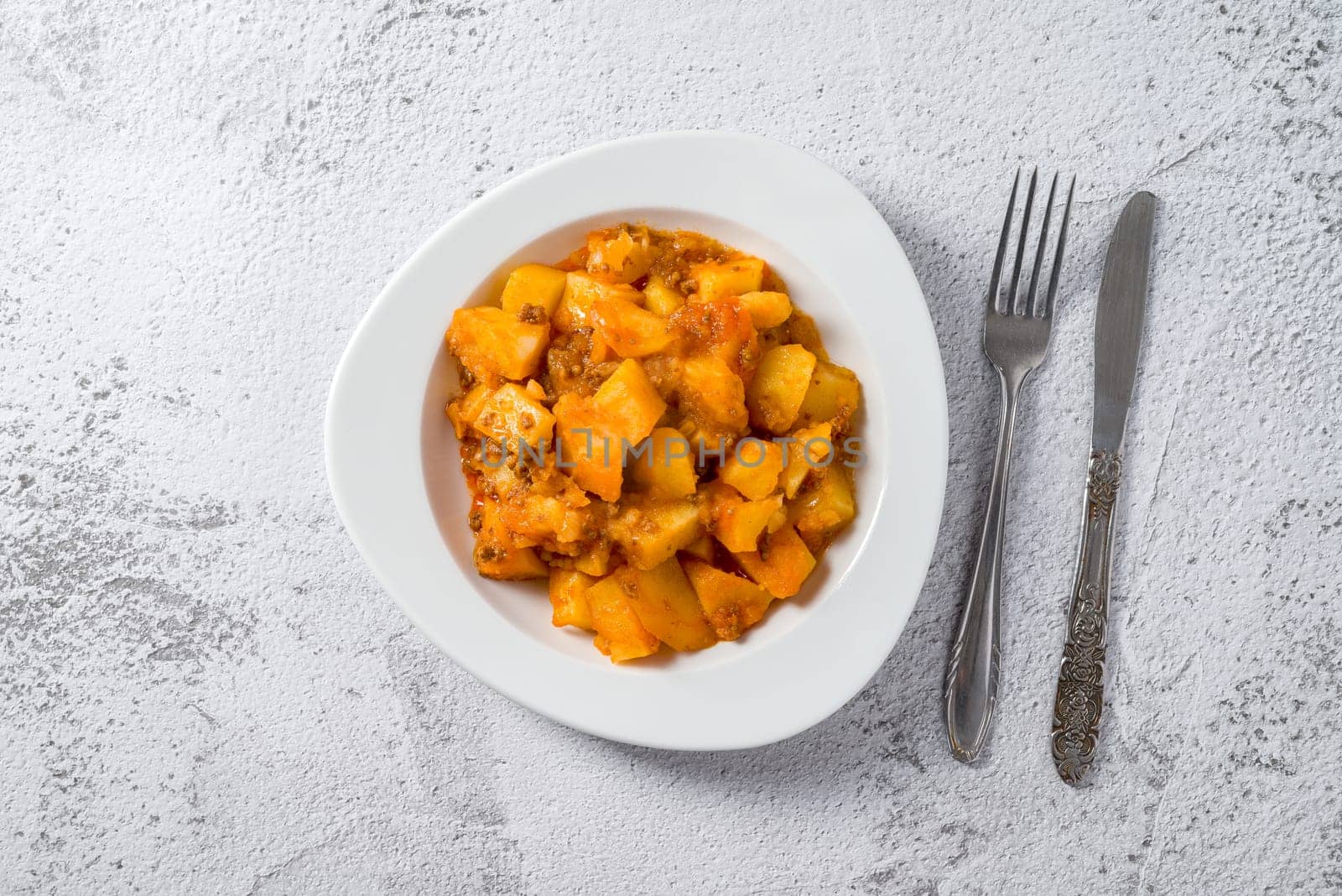 Minced meat and potato dish on white porcelain plate on stone table by Sonat