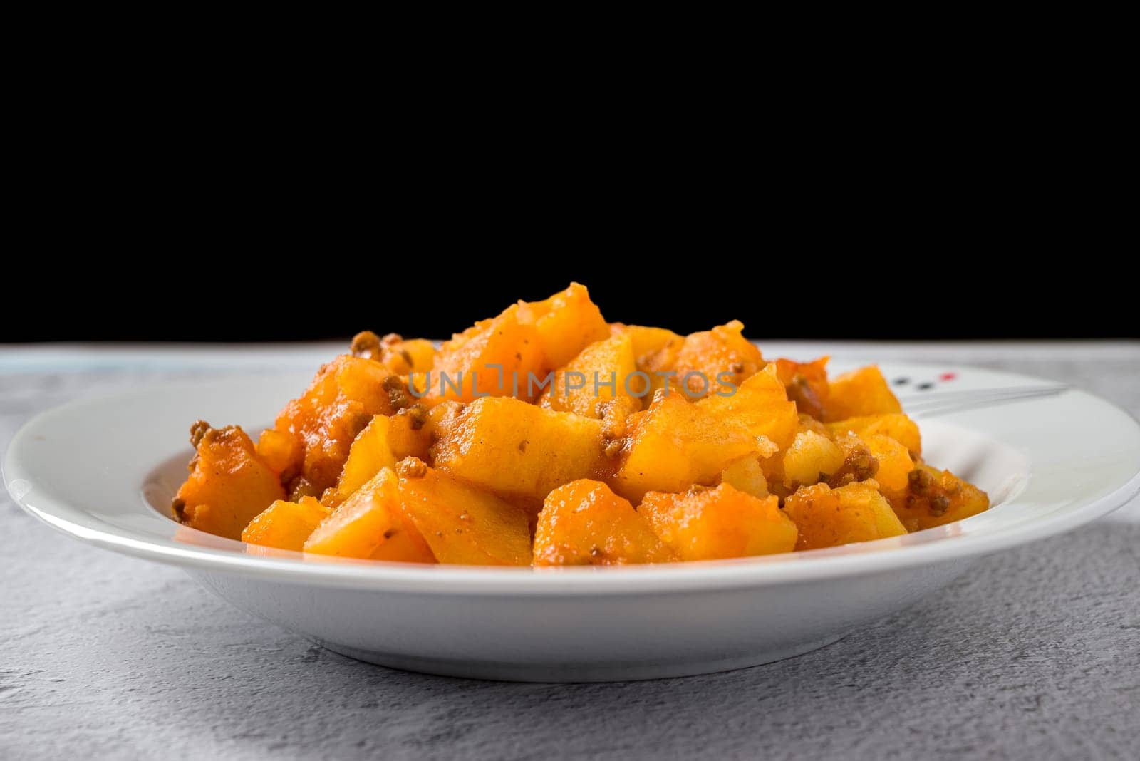 Minced meat and potato dish on white porcelain plate on stone table by Sonat