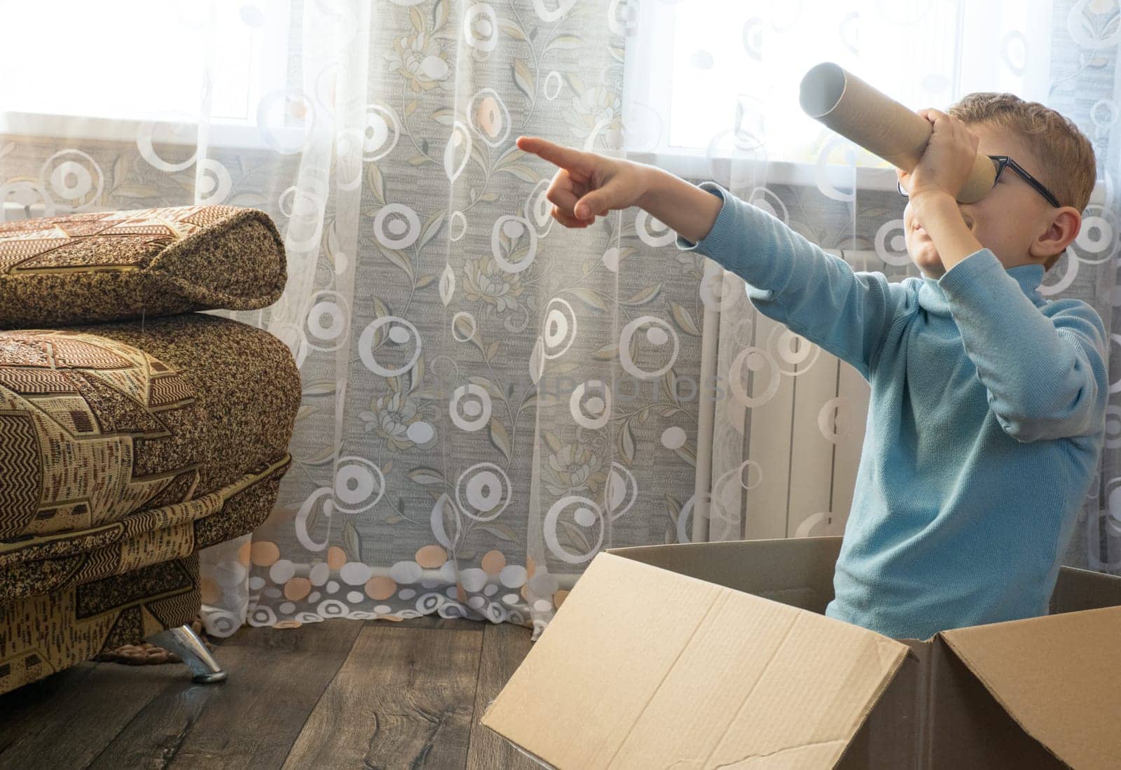 Playful cheerful child, boy looking into a cardboard tube, sitting in a box.