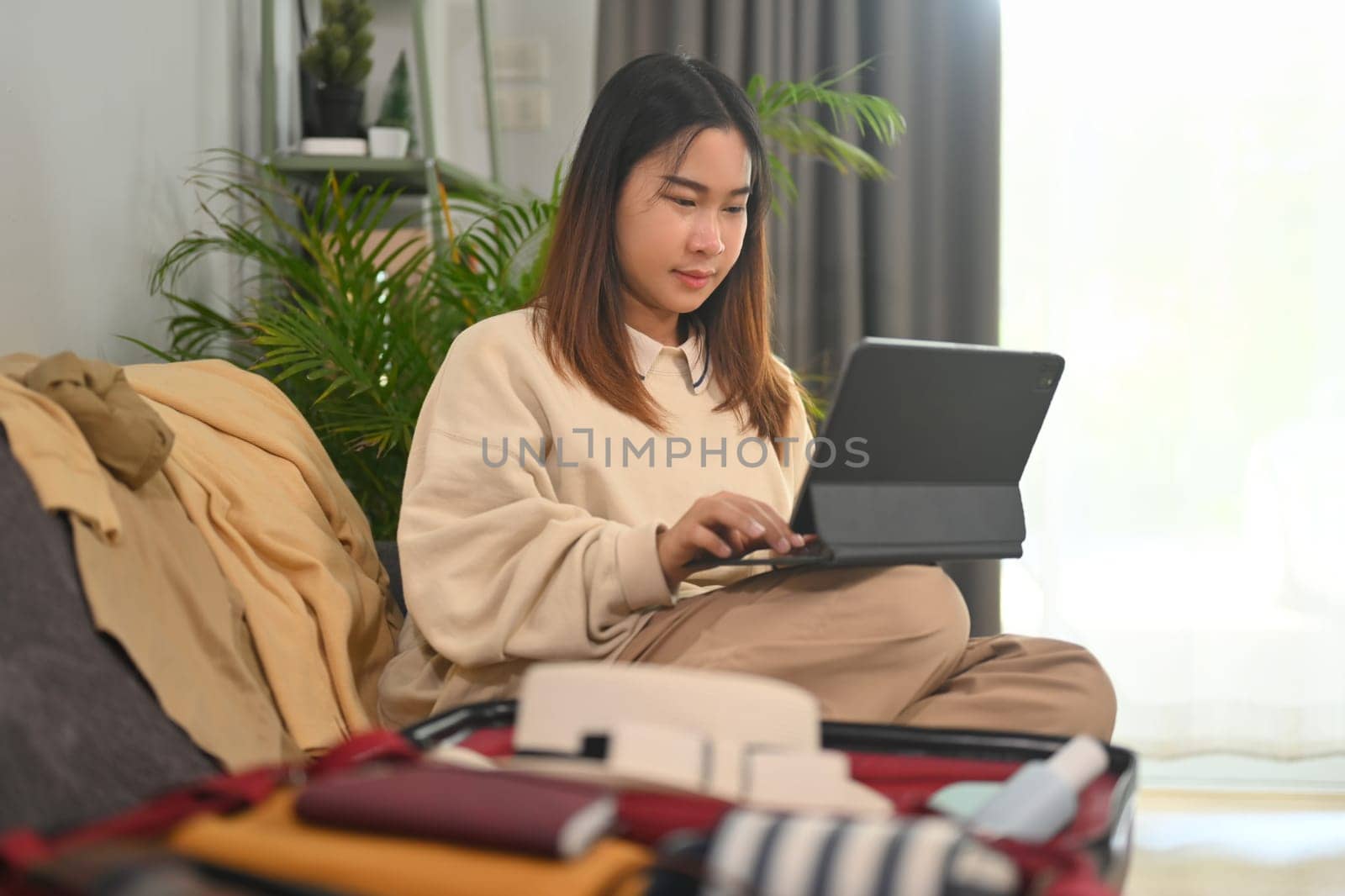 Young woman planning for trip with digital tablet, getting ready for holidays travel trip in living room.