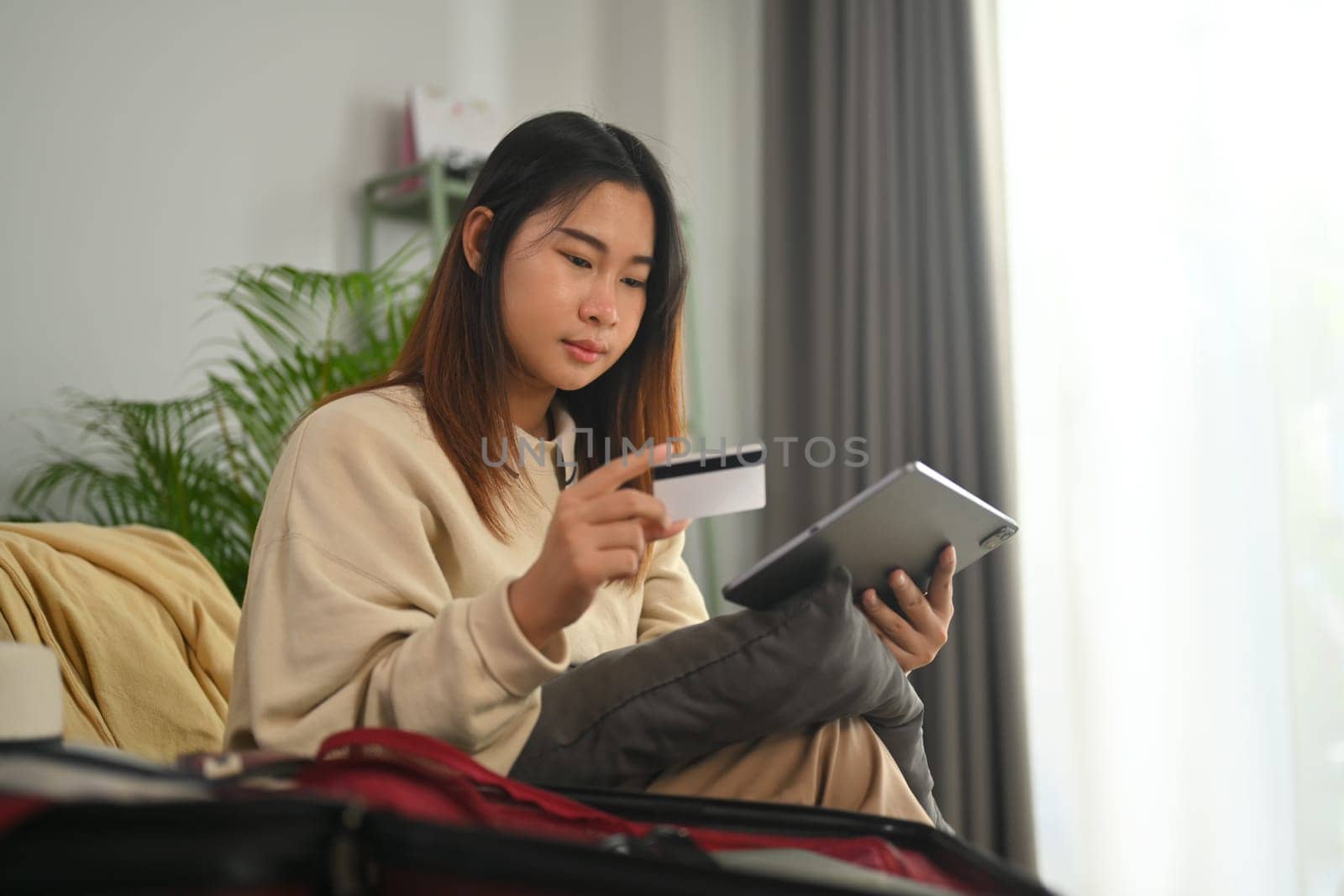 Young woman holding credit card and using digital tablet while transferring money or booking hotel room by prathanchorruangsak