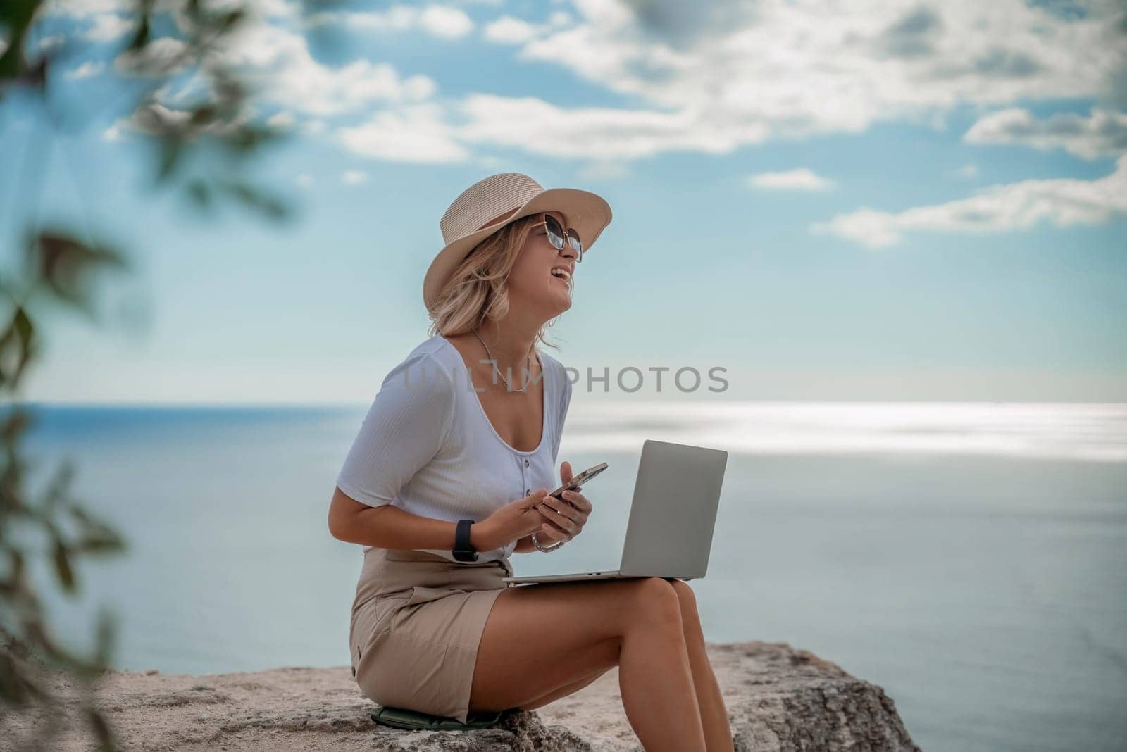 Freelance women sea working on the computer. Good looking middle aged woman typing on a laptop keyboard outdoors with a beautiful sea view. The concept of remote work