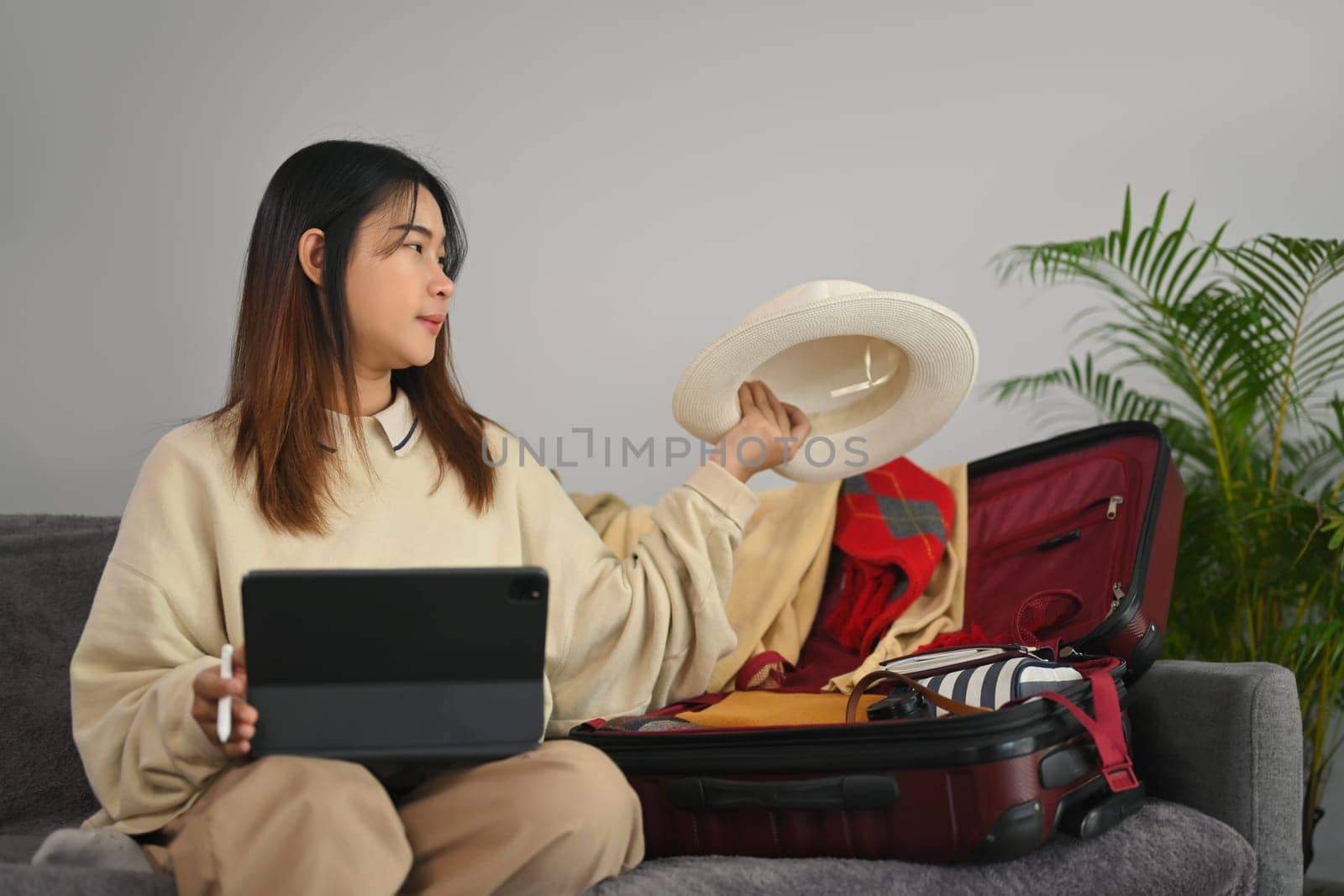 Smiling young woman preparing luggage for travel trip and booking hotel reservation on digital tablet.