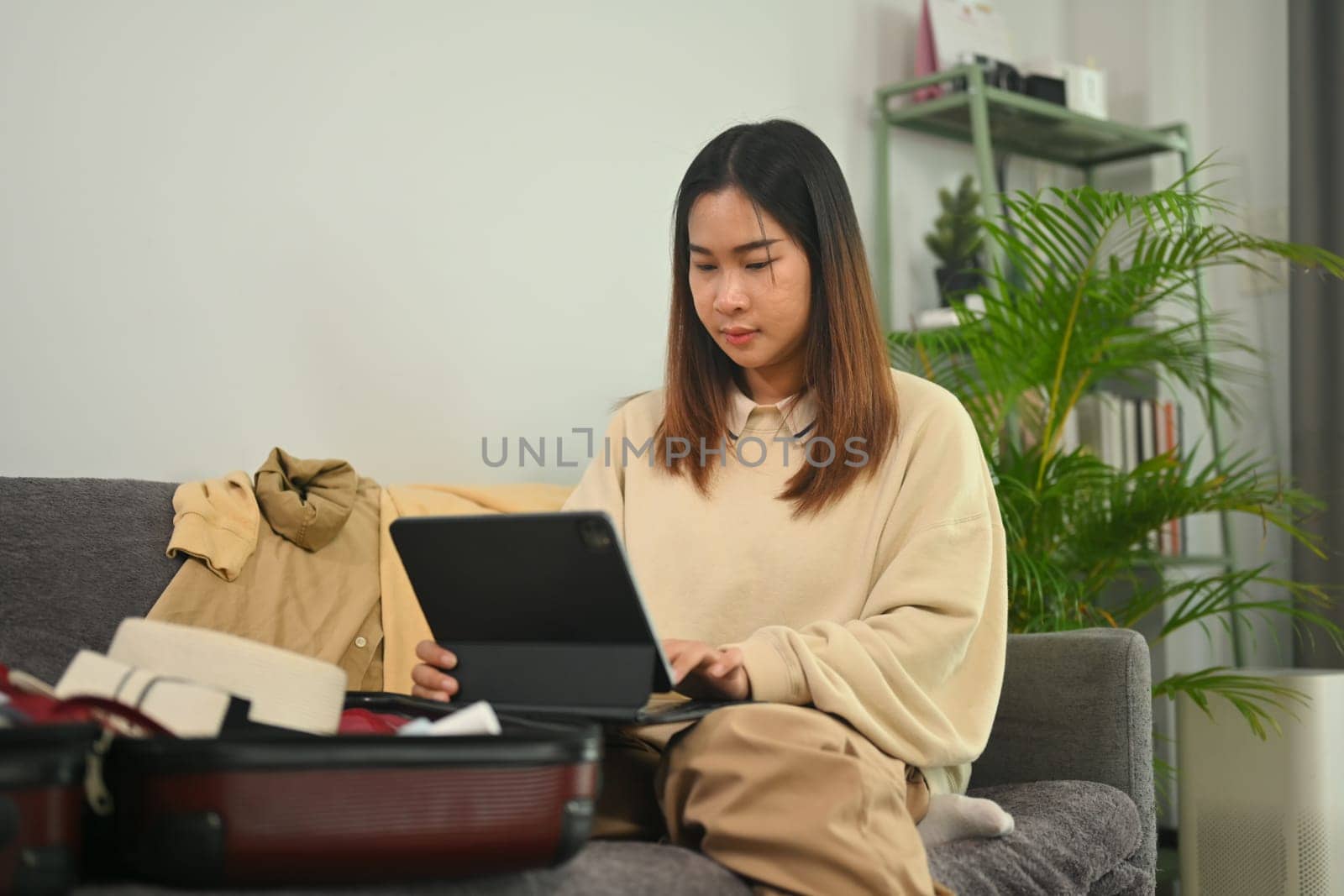 Young woman planning for trip with digital tablet, getting ready for a vacation in living room.