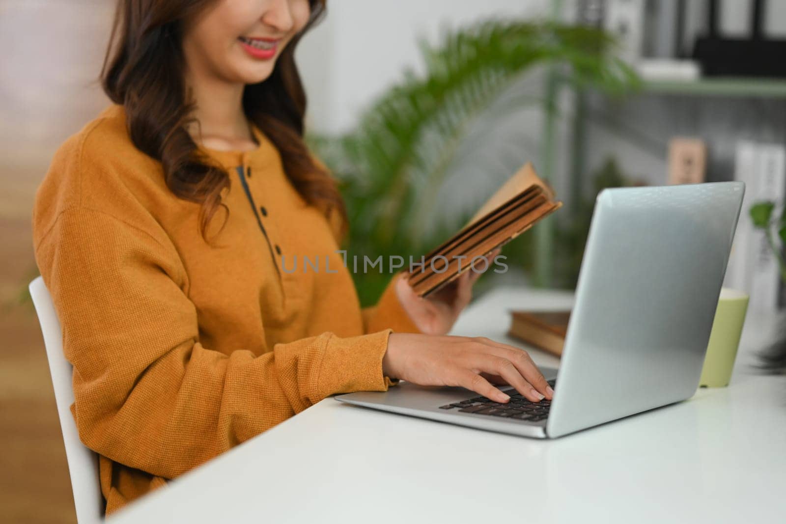 Cropped shot casual young woman browsing internet on laptop at home by prathanchorruangsak