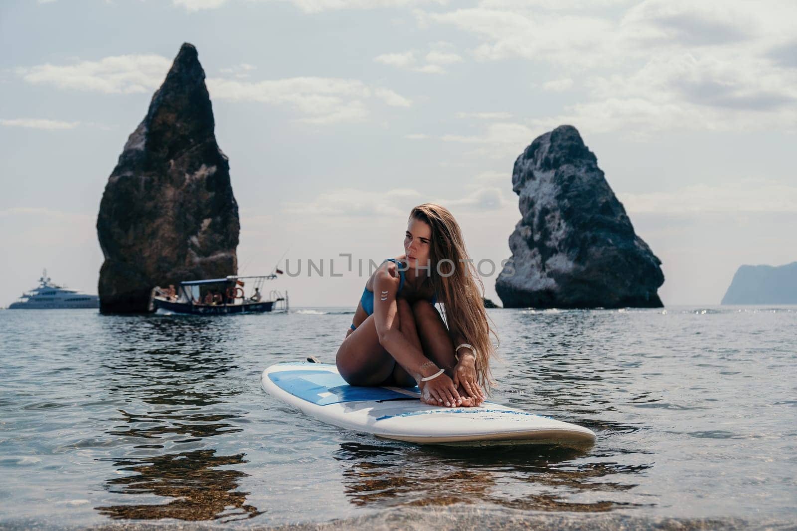 Close up shot of beautiful young caucasian woman with black hair and freckles looking at camera and smiling. Cute woman portrait in a pink bikini posing on a volcanic rock high above the sea