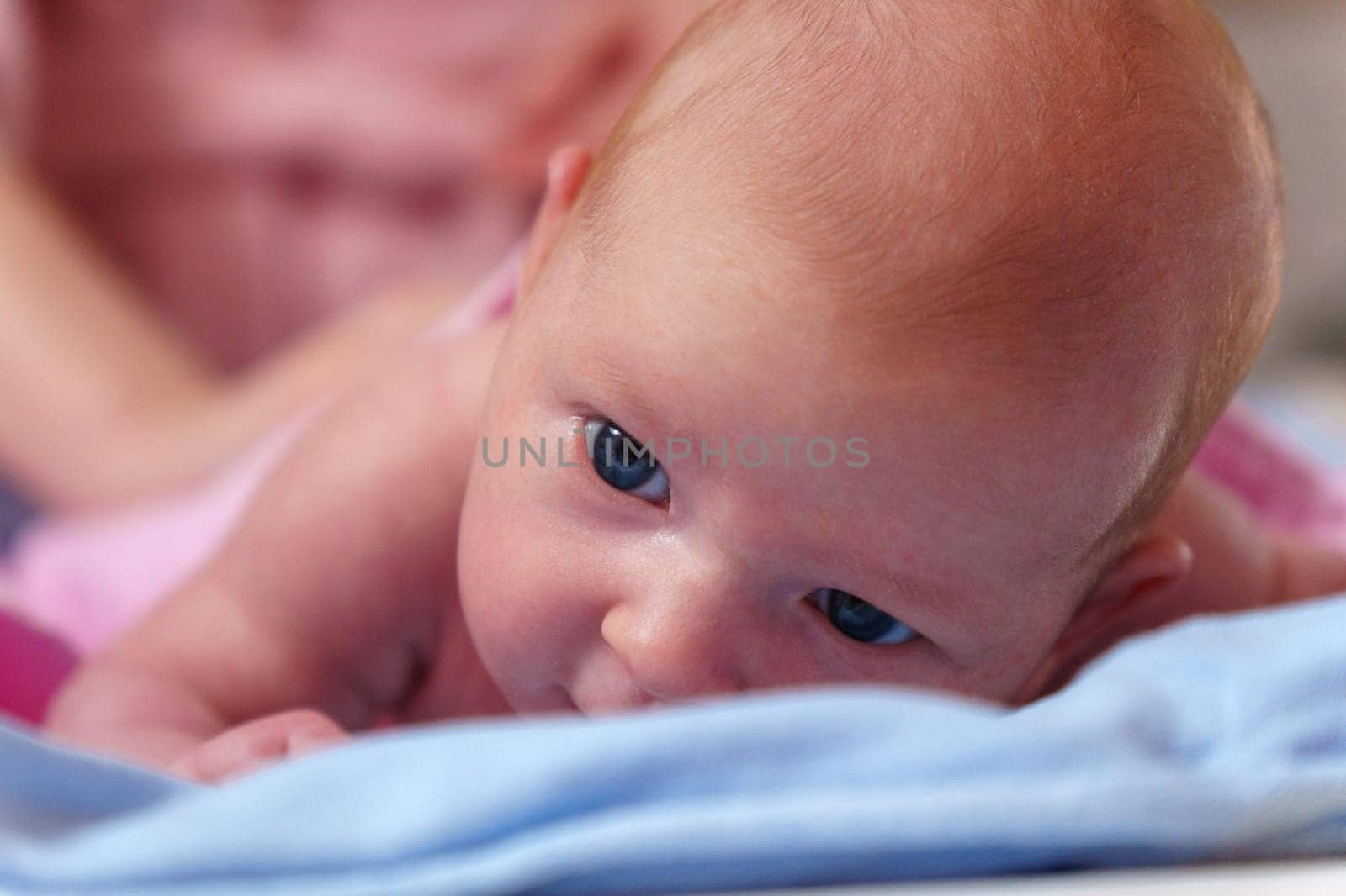 Newborn baby, at the tender age of two months, lies comfortably while curiously looking at the world around with bright, expressive eyes.