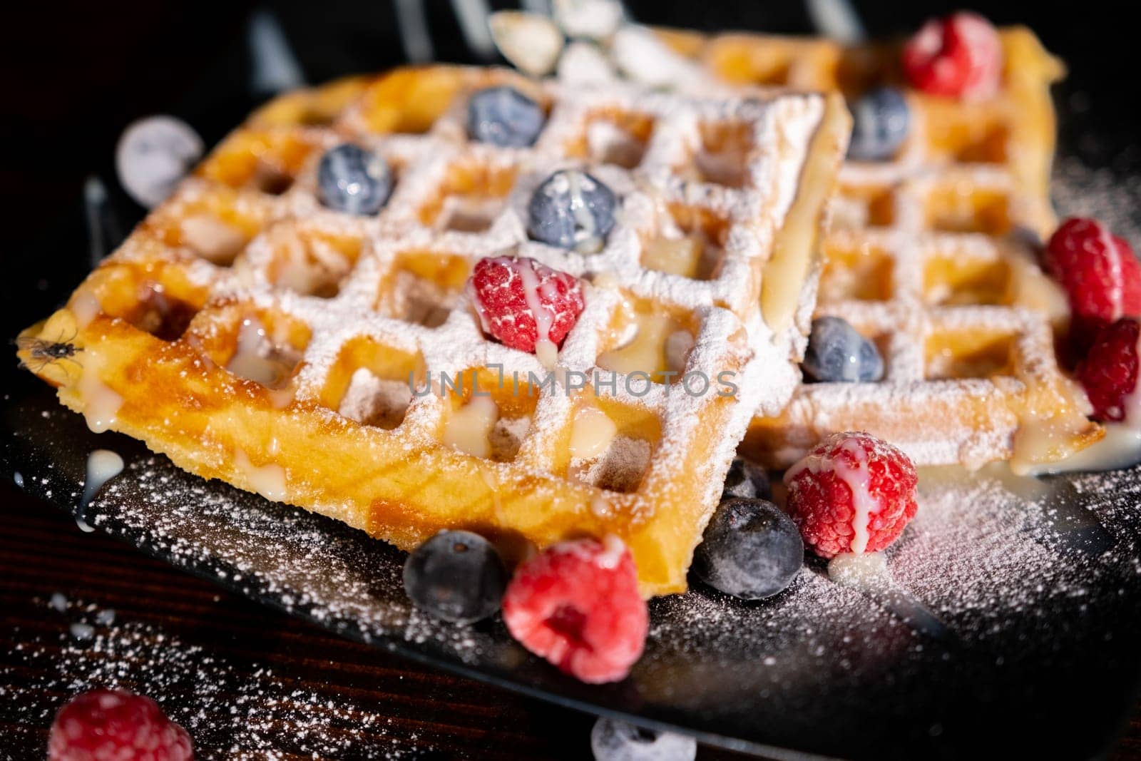 Belgian French waffles close-up with berries, blueberries athens raspberries blueberries sprinkled with powdered sugar, condensed milk, side view isolated on black background. Sweet breakfast dessert