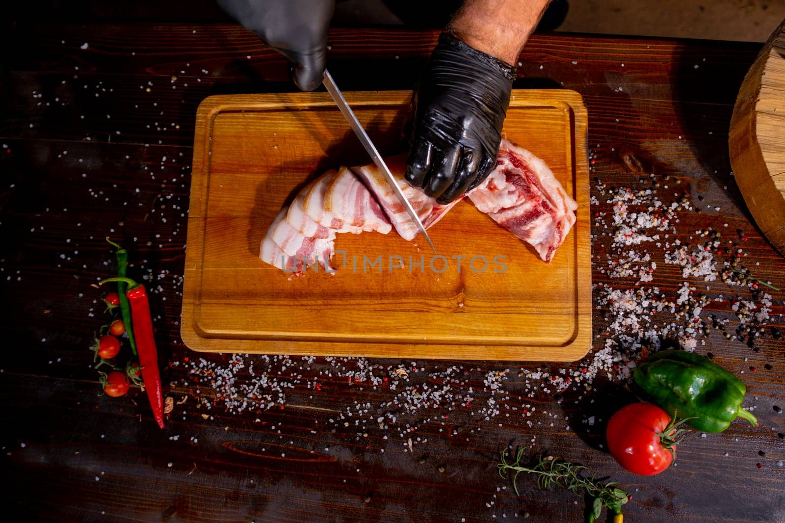 Salted Lard, Raw Pork with Spices on Wooden Cutting Board Studio Photo. A butcher in black gloves thinly slices lard. High quality photo