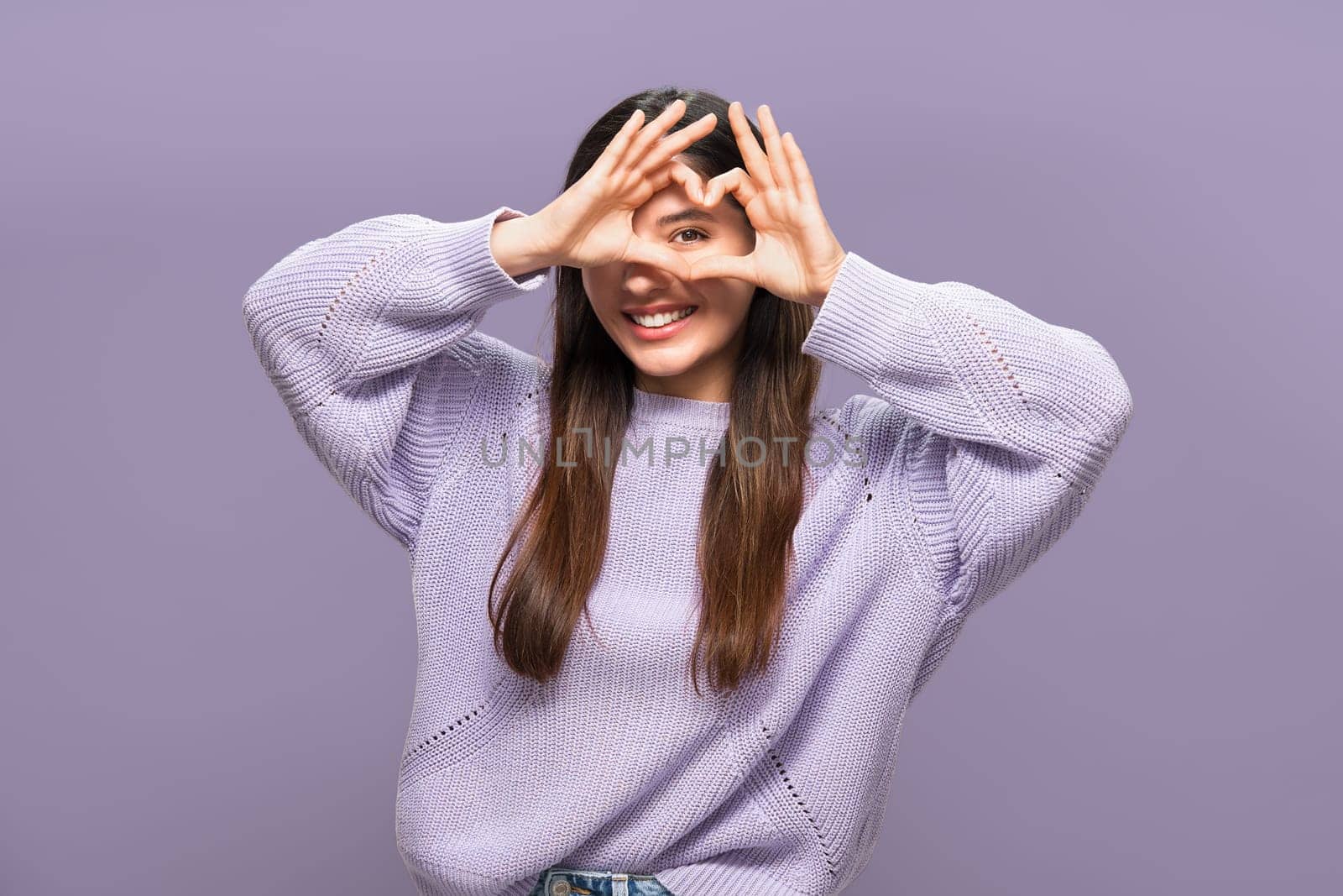 In love cheerful attractive multiracial woman in purple making a heart with her hands.