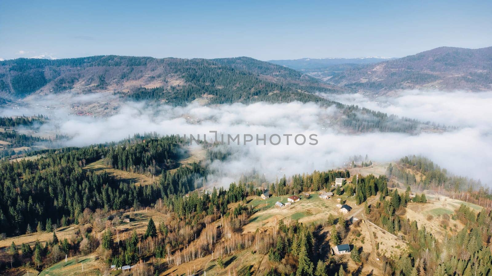 Mountains in clouds at sunrise in spring. Aerial view of mountains with green trees in fog. Beautiful landscape with hills, forest, sky. Top view from drone of mountain valley in low clouds