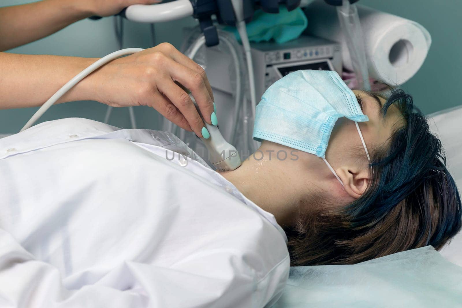 A young girl undergoes an ultrasound of the thyroid gland. patient wearing a mask. Doctor conducting ultrasound examination of woman in clinic, closeup. Soft focus