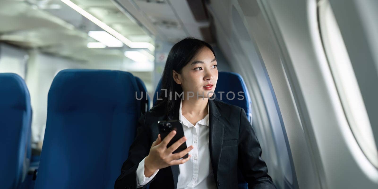 Beautiful Asian businesswoman using mobile phone in aeroplane. working, travel, business concept.