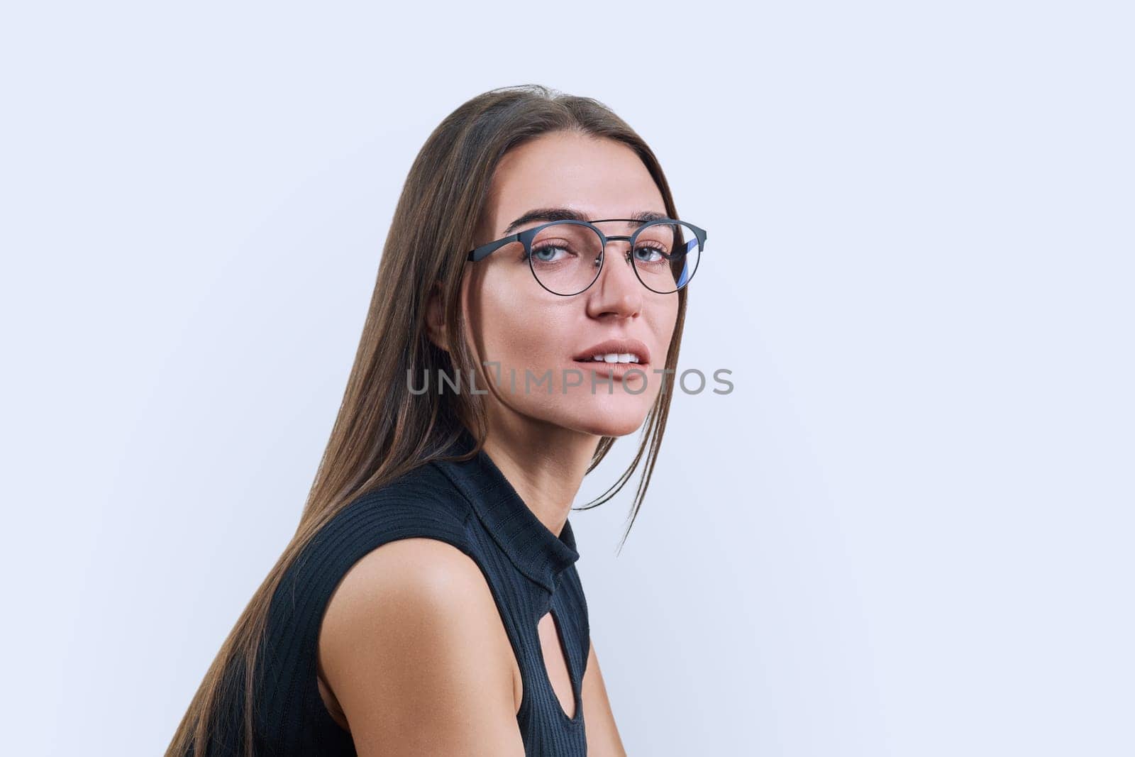 Headshot portrait of young beautiful woman in fashionable trendy glasses on white studio background. Close-up of face of fashionable female looking at camera. Beauty, fashion, style