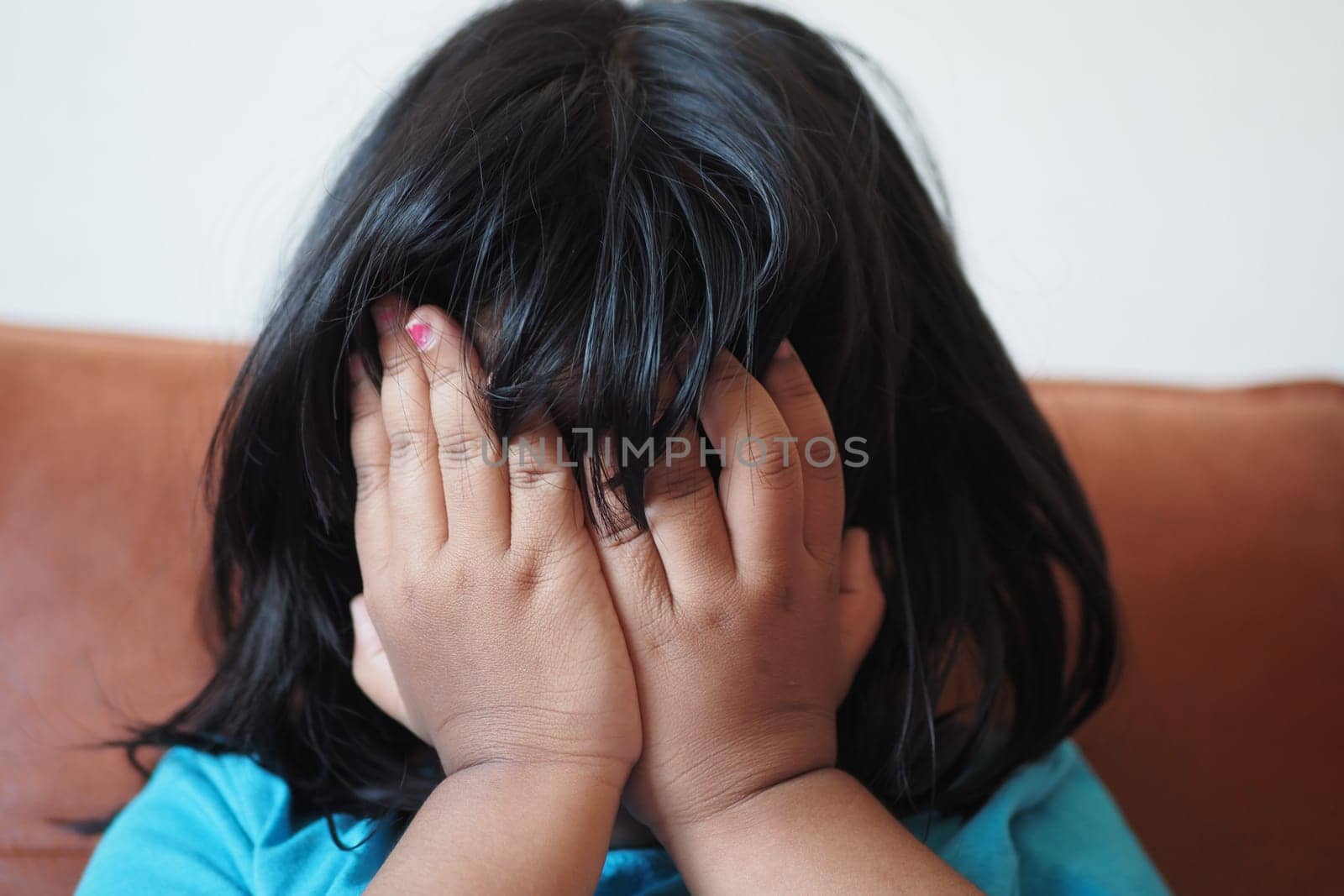 a upset child girl cover her face with hand .