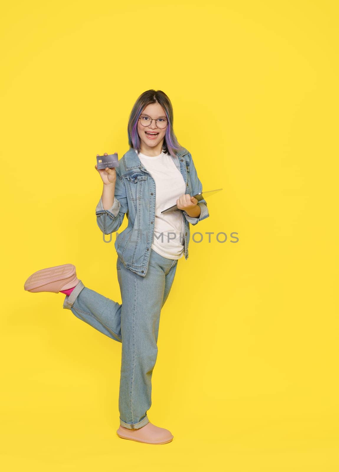 Happy Customer Show A Bank Credit Card, Ready To Make Purchase Online In Web Store From Tablet Pc. Girl In Casual Closes Isolated On Yellow. High quality photo