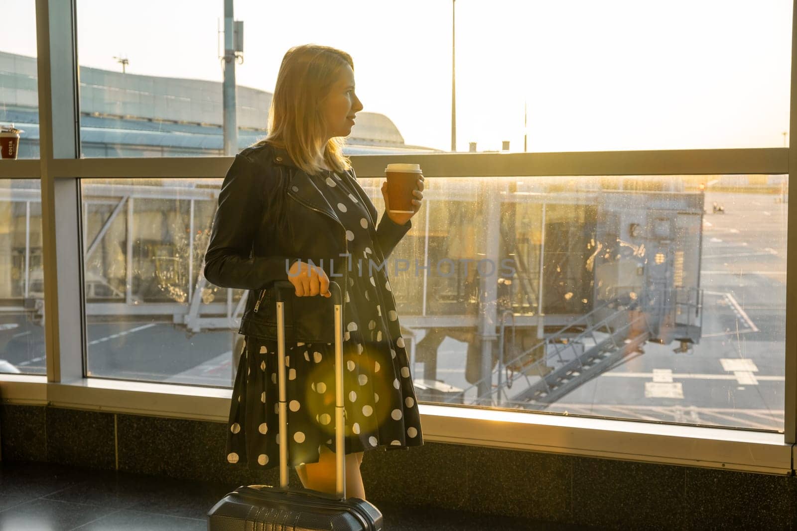 A young woman, holding a cup of coffee is ready for boarding with her suitcase by vladimka