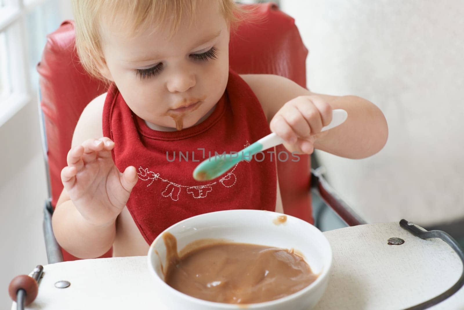 High chair meal, baby and eating spoon in a house with diet, nutrition and child, wellness or development. Food, messy eater and boy kid curious about breakfast cereal, playing or learning at home.