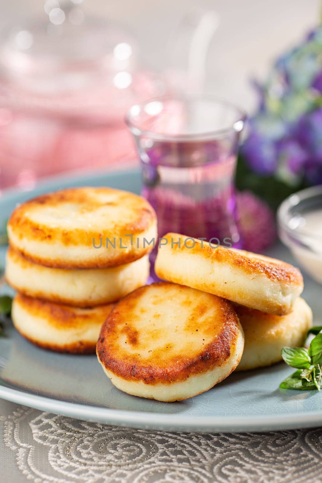 Fried cottage cheese pancakes syrniki served with sour cream and flower tea on a blue dish. by Gravika