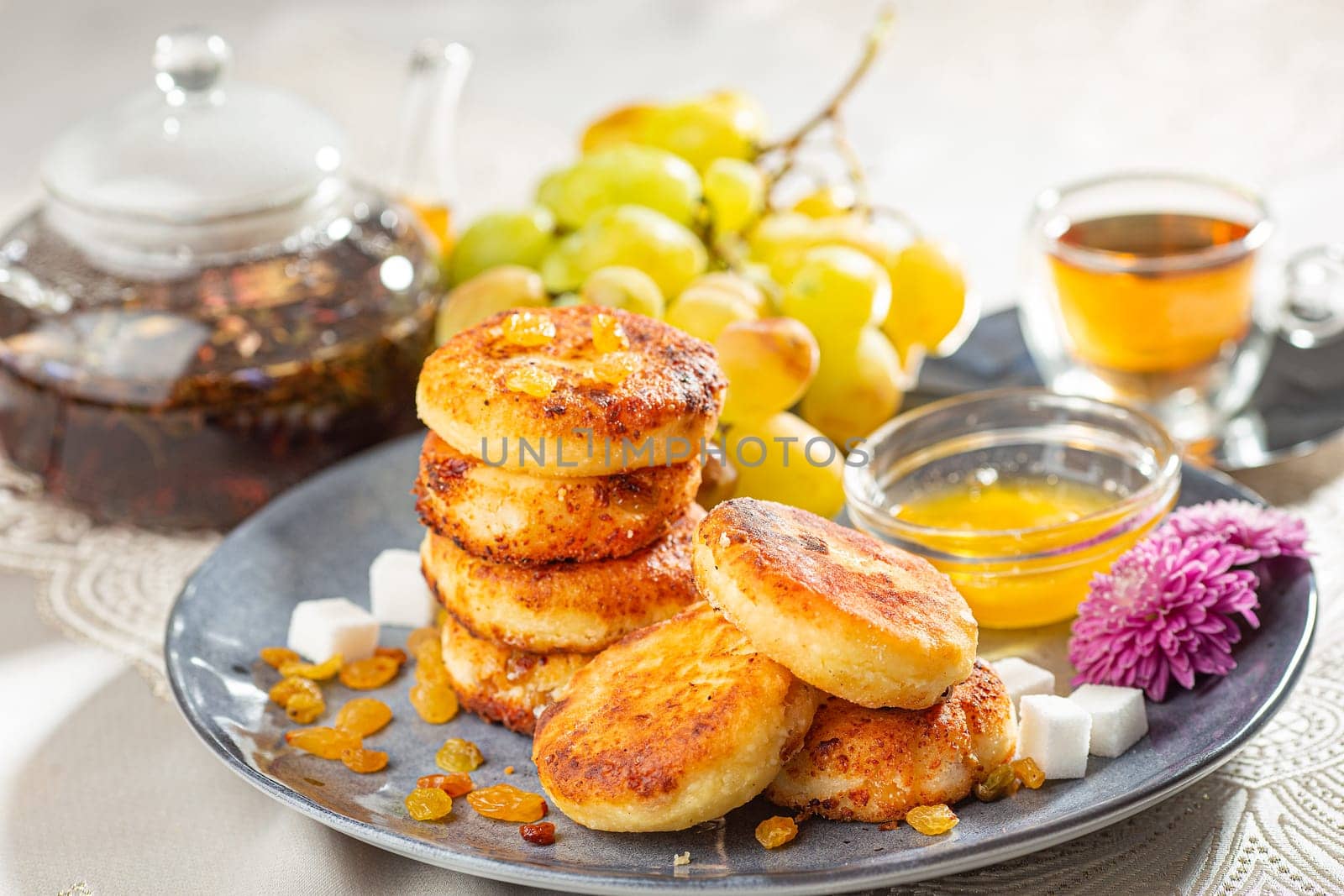 Fried cottage cheese pancakes syrniki with raisins, grapes and honey on a blue dish served with black tea. by Gravika