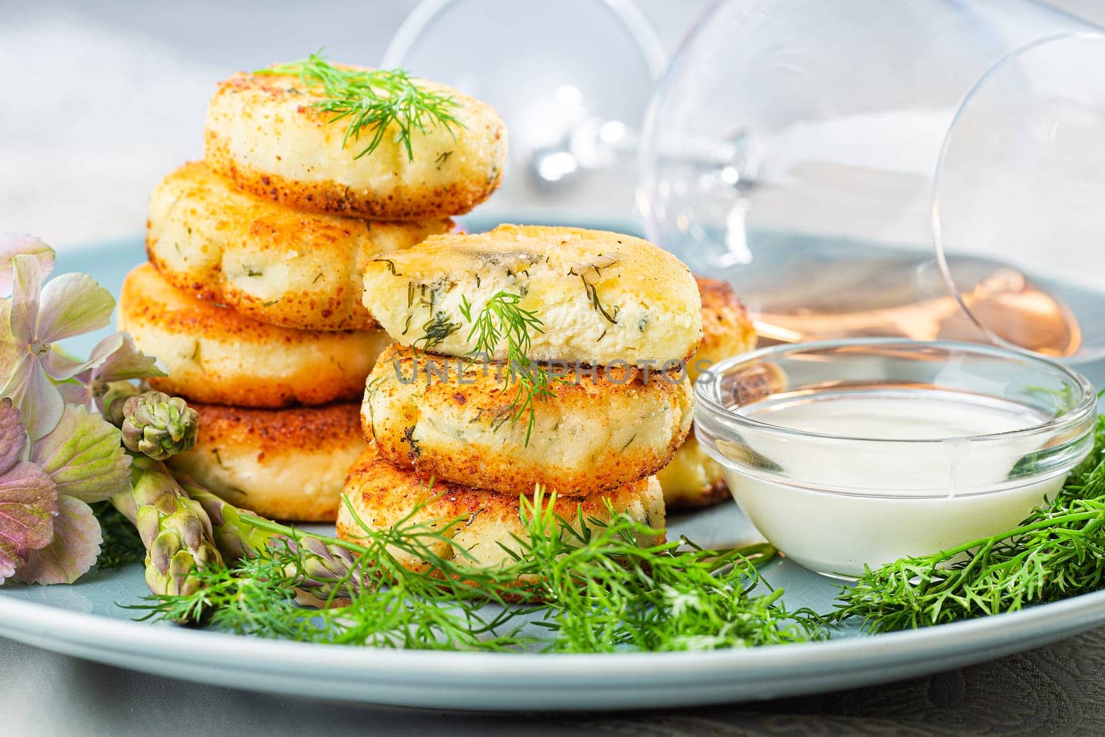 Fried cottage cheese pancakes syrniki with dill and asparagus on a blue plate served with sour cream and wine. by Gravika