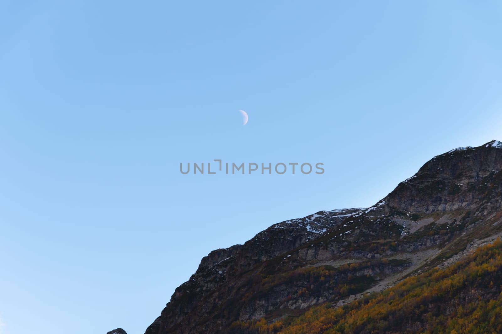 Clear daytime blue sky, mountains and waning white moon.