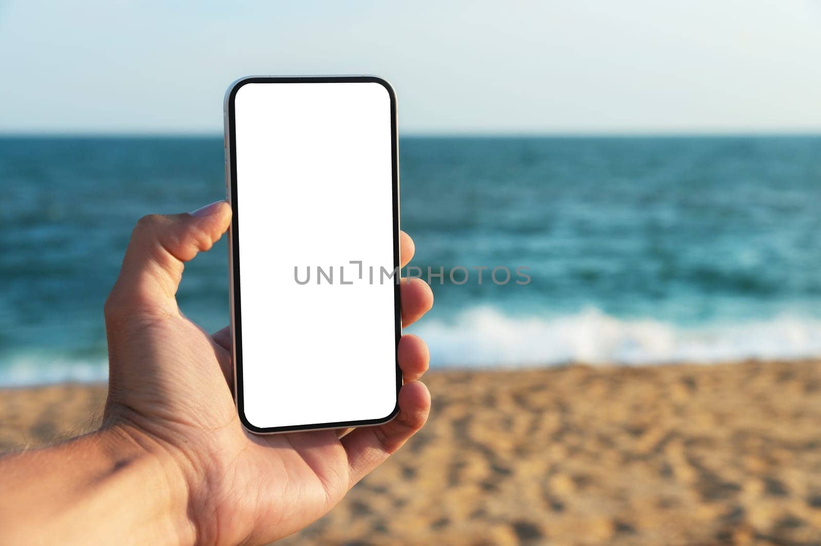 A man with an empty mobile phone by the sea, close-up. Mockup on a smartphone in a person's hand.