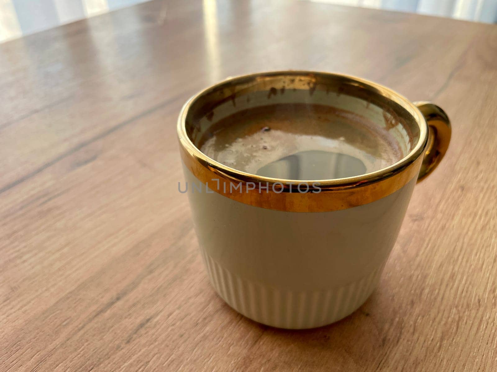 Morning coffee in a green cup with a golden rim stands on a wooden table. High quality photo